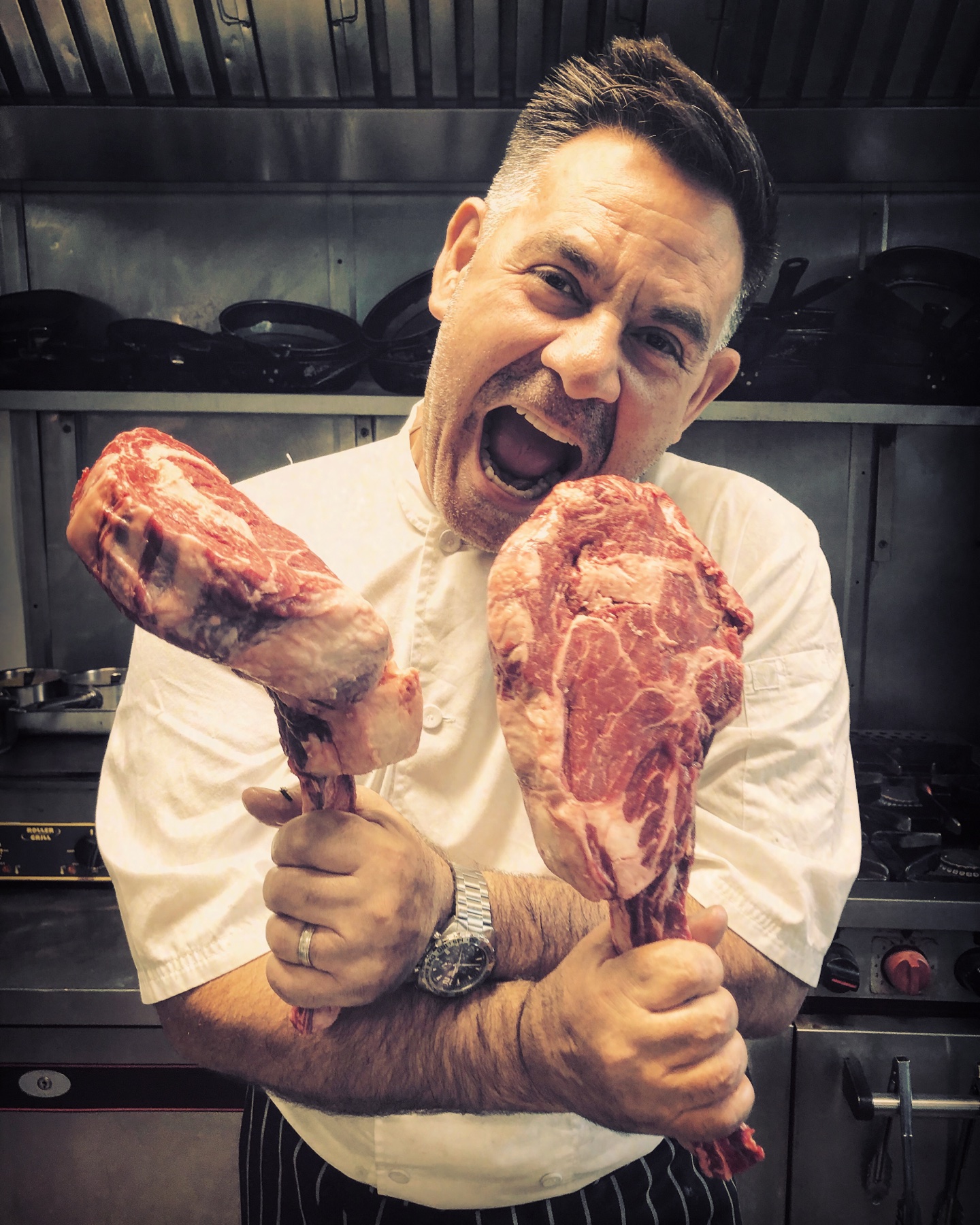 Head Chef George Jiojioras holding two cuts of meat in the kitchen